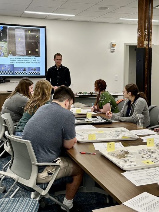 Professor and students around a table with artifact trays.